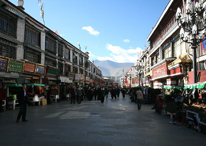The long perspective of Barkhor Street in Lhasa with distant mountains visible under a clear sky.