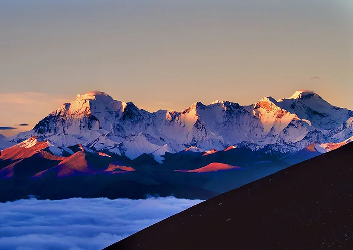 Snow-capped Himalayan peaks glow orange and pink at sunset above a thick sea of white clouds in the Shigatse region of Tibet.