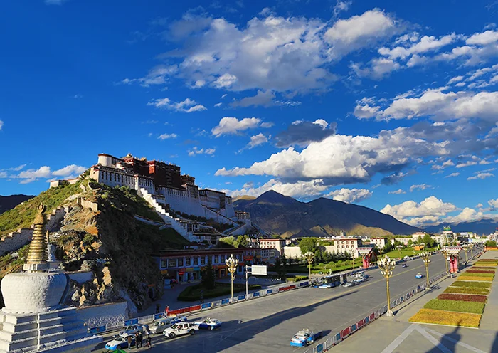 Classic view of Potala Palace from Chakpori Hill featuring white stupas and the main road in Lhasa.