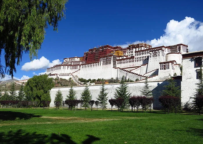 The Potala Palace rising above lush green trees and park lawns on a clear day in Lhasa.