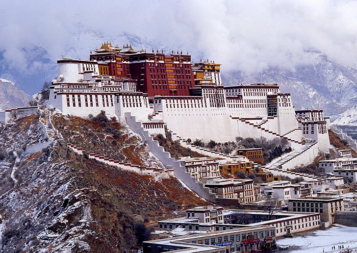 The Potala Palace covered in snow with heavy clouds and misty mountains in the background.