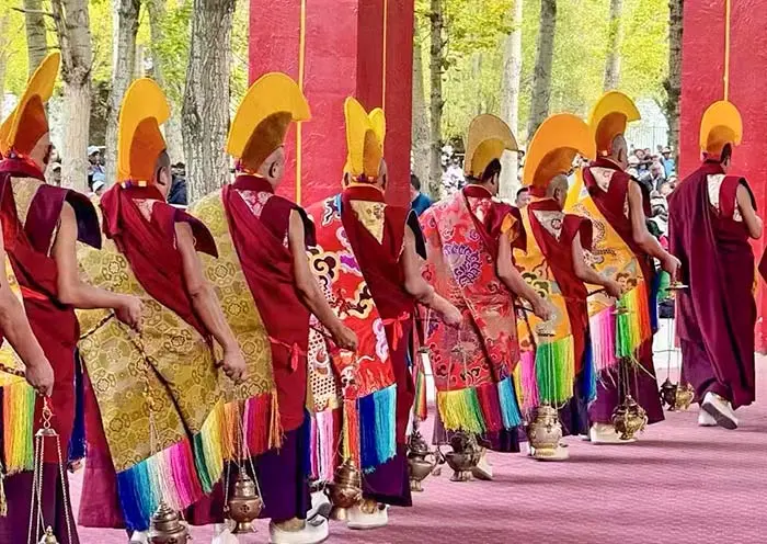 A line of Tibetan monks wearing traditional yellow hats and ceremonial robes during a religious ritual in Lhasa.